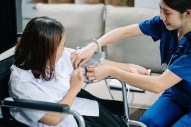 Asyalı genç bayan hemşire tekerlekli sandalyedeki kadın hastanın kan basıncını ölçüyor. Tıbbi bir ortamda özen, şefkat ve profesyonellik gösterme.