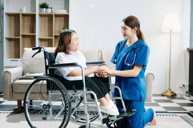 Tekerlekli sandalyede el ele tutuşan genç bir bayan hemşire. Tıbbi bir ortamda özen, şefkat ve profesyonellik gösterme.