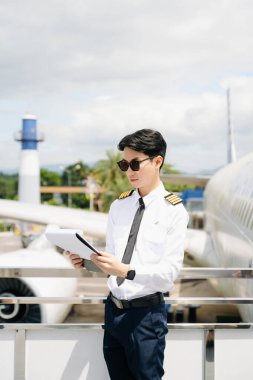 Üniformalı Asyalı genç pilot uçağın dışında duruyor.