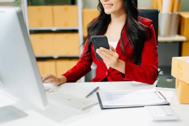 Küçük işletme KOBİ 'si kurun. İş kadını bilgisayar ve akıllı telefonu kullanarak online alışveriş siparişini alıp kontrol ederek ofiste ürün hazırlıyor.