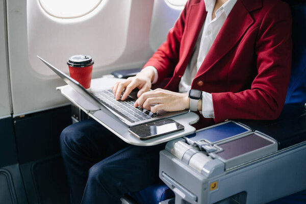 Портрет успешного азиатского бизнесмена в официальном костюме на самолете, сидящем в бизнес-классе с помощью ноутбука 