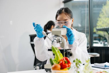 Laboratuvar önlüklü iki kadın gıda bilimcisi, örnek alıyor ve modern bir laboratuvar ortamında gıda güvenliğini ve kalitesini analiz ediyorlar.