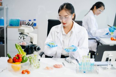 Laboratuvar önlüklü iki kadın gıda bilimcisi, örnek alıyor ve modern bir laboratuvar ortamında gıda güvenliğini ve kalitesini analiz ediyorlar.