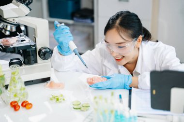 Laboratuvar önlüklü gülümseyen kadın gıda bilimcisi, numuneleri test ediyor ve modern bir laboratuvar ortamında gıda güvenliğini ve kalitesini analiz ediyor.