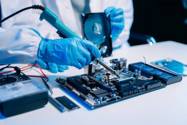 Teknisyenin masasında sabit diskle çalışan bir tamirci ve bir bilgisayar anakart parçası. Veri, donanım ve bilgi teknolojisi kavramı 