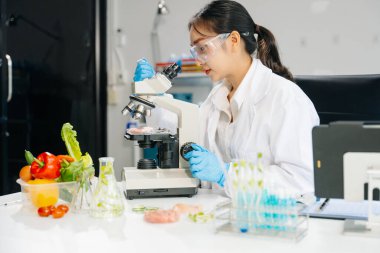 Laboratuvar önlüklü kadın gıda bilimcisi, numuneleri test ediyor ve modern bir laboratuvar ortamında gıda güvenliği ve kalitesini analiz ediyor.