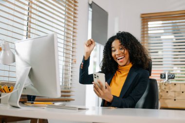 Afrikalı iş kadını yaptığı işten memnun ve mutlu. Ofisteki akıllı telefondan video görüşmesi yapıyor.