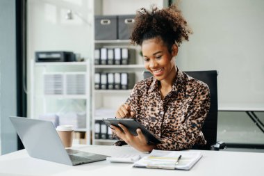 Genç Afrikalı Amerikalı iş kadını ofiste tablet, dizüstü bilgisayar ve belgelerle çalışıyor. 