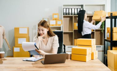 İki Asyalı kadın online siparişleri kontrol eder, ürün satar, ev ofisinden teslimat için kutu paketlerler. Küçük işletmeler kurmak, KOBİ sahipleri kavramı. 