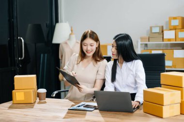 İki Asyalı kadın online siparişleri kontrol eder, ürün satar, ev ofisinden teslimat için kutu paketlerler. Küçük işletmeler kurmak, KOBİ sahipleri kavramı. 