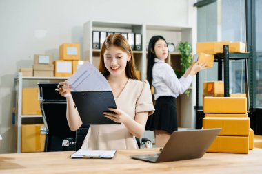 İki Asyalı kadın online siparişleri kontrol eder, ürün satar, ev ofisinden teslimat için kutu paketlerler. Küçük işletmeler kurmak, KOBİ sahipleri kavramı. 