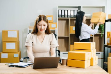 İki Asyalı kadın online siparişleri kontrol eder, ürün satar, ev ofisinden teslimat için kutu paketlerler. Küçük işletmeler kurmak, KOBİ sahipleri kavramı. 