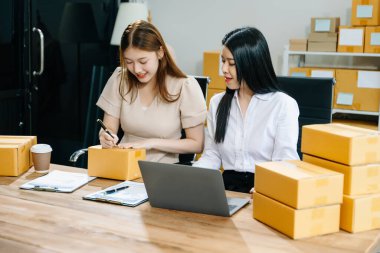 İki Asyalı kadın online siparişleri kontrol eder, ürün satar, ev ofisinden teslimat için kutu paketlerler. Küçük işletmeler kurmak, KOBİ sahipleri kavramı. 