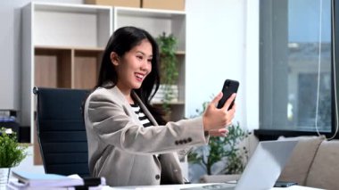 Ofiste video görüşmesi yapmak için akıllı telefon kullanan bir kadın.