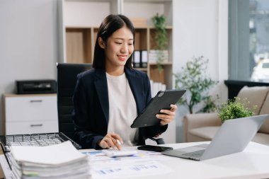 Genç ve güzel bir kadın çalıştığı yerde bilgisayarını ve dijital tabletini kullanıyor..