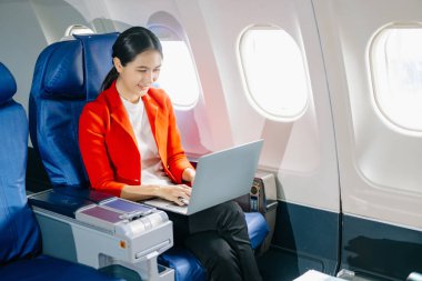 Uçaktaki çekici Asyalı kadın yolcu dizüstü bilgisayarla çalışırken rahat koltukta oturuyor.