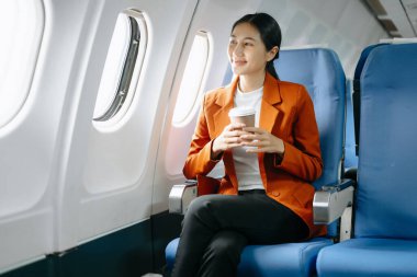 Başarılı bir Asyalı iş kadını portresi ya da resmi takım elbiseli bir girişimci birinci sınıfta oturmuş kahve içiyor.