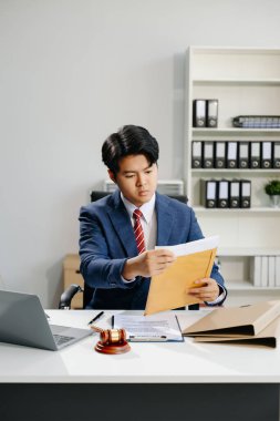 Belgelerle çalışan Asyalı genç avukat, modern ofisteki masasında pirinç tartı..