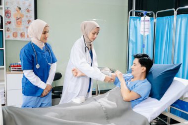 Kadın doktorlar hastane koğuşundaki hastaya kan basıncını ölçüyorlar. Profesyonellik ve takım çalışması sergiliyorlar.