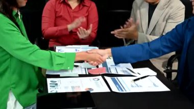 Ofiste yapılan toplantıda iş adamları grafiklerle sunum yapıyor ve el sıkışıyorlar 