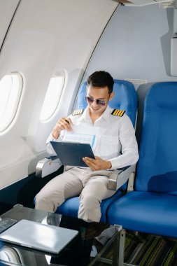 Üniformalı Asyalı erkek pilot ve güneş gözlüğü yolcu koltuğunda uçuş planlarını kontrol ediyor. 
