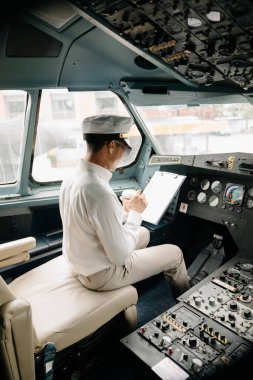 Üniformalı Asyalı özgüvenli erkek pilot uçak kokpitinin içinde oturuyor.