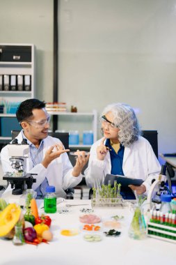 Erkek ve kadın Asyalı bilim adamları, mikroskop ve laboratuvar ekipmanları kullanarak gıda araştırmaları yapıyorlar, gıda bilimi ve biyoteknoloji alanında yenilik sergiliyorlar.