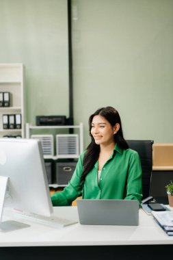 gülümseyen Asyalı iş kadını iş yerinde bilgisayar kullanıyor..