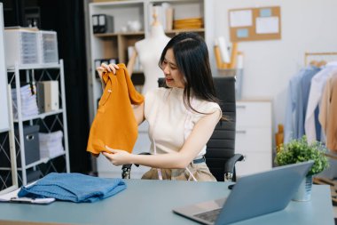 Asyalı terzi dizüstü bilgisayar kullanarak terzide elbise dikmeye çalışıyor.