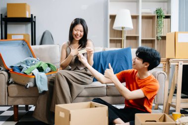 Asyalı genç ve çekici bir çift yeni eve taşınıyor ve ellerinde alışveriş için kredi kartı var. Genç evli Asyalı eve taşınıyor ve baş parmağını kaldırıyor.