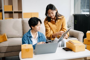 Başlangıçta küçük işletme KOBİ 'si, kanepede oturan iki kadın işletme sahibi, paketleri hazırlamak için çevrimiçi siparişleri almak ve kontrol etmek için dizüstü bilgisayar kullanıyorlar.. 