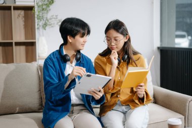 Okul projesinde çalışan iki genç Asyalı kız üniversite öğrencisi kanepede birlikte tablet bilgisayar kullanıyorlar.. 