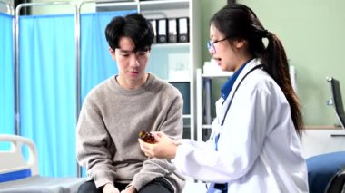 Asyalı kadın doktor hastane yatağında erkek hastaya nasıl hap içileceğini anlatıyor.  