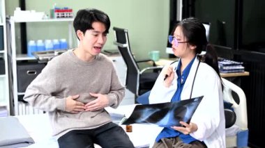 Hastanedeki semptomlarını anlatırken Asyalı kadın doktor hastanın röntgenini kontrol ediyor. 