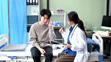 Hastane yatağındaki Asyalı erkek hasta semptomlarını hastanedeki kadın doktora açıklar.