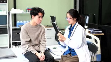 Asyalı kadın doktor hastane yatağında erkek hastaya nasıl ilaç içileceğini anlatıyor. 