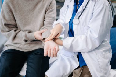 Kadın doktor hastanede nabzını kontrol ederken erkek hastanın orta bölümü yatakta oturuyor.