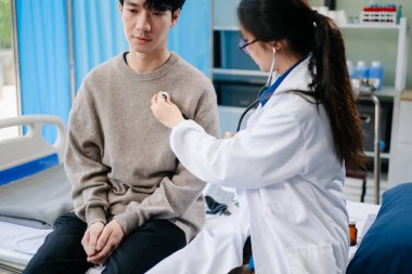 Erkek hastayı yatakta ve hastanede kontrol etmek için steteskop kullanan Asyalı kadın doktor.