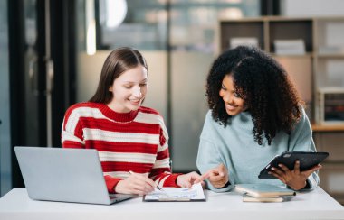 Modern ofiste dizüstü bilgisayar ve dijital tabletle çalışan iki iş kadını