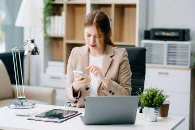 Ofiste çalışırken dizüstü bilgisayar ve akıllı telefon kullanan kadın girişimci 