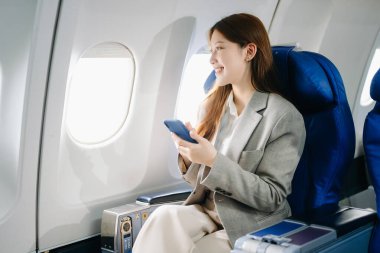 Genç Asyalı kadın yolcu akıllı telefon kullanarak rahat koltukta oturuyor. 