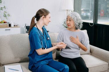  Genç bakıcı doktor yaşlı hastayı muayene ediyor. Kadın terapist ve yaşlı kadın kanepede oturuyor. Tıbbi servis kavramı