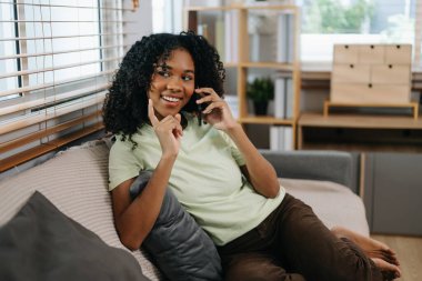 Genç Afrikalı kadın evdeki kanepede akıllı telefondan konuşuyor.