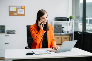 Diz üstü bilgisayar kullanan ve ofiste çalışırken akıllı telefondan konuşan bir girişimci. 