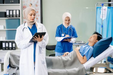 Hastane koğuşundaki bir hastaya bakım sunan tesettürlü doktorlar takım çalışması, profesyonellik ve şefkatli bir sağlık ortamı sunuyorlar..