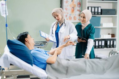 Hastane koğuşundaki bir hastaya bakım sunan tesettürlü doktorlar takım çalışması, profesyonellik ve şefkatli bir sağlık ortamı sunuyorlar..