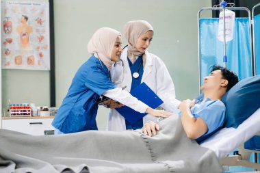Hastane koğuşundaki bir hastaya bakım sunan tesettürlü doktorlar takım çalışması, profesyonellik ve şefkatli bir sağlık ortamı sunuyorlar..