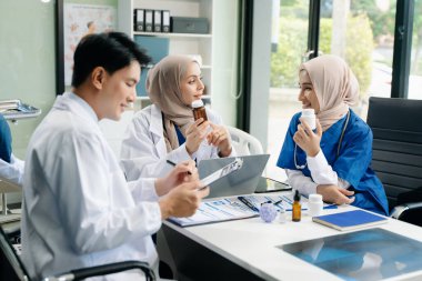 Genç Müslüman doktor ve Asyalı bayan ekip hastanede hastalar hakkında konuşurken tartışıyor ve gülümsüyor.