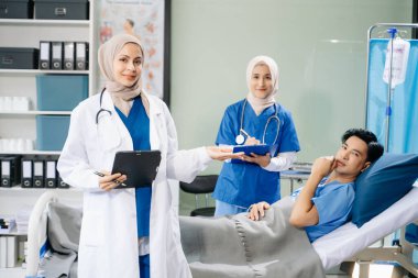 Hastane koğuşundaki bir hastaya bakım sunan tesettürlü doktorlar takım çalışması, profesyonellik ve şefkatli bir sağlık ortamı sunuyorlar..