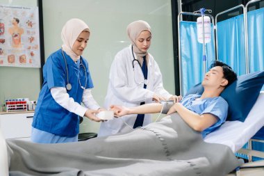 Hastane koğuşundaki bir hastaya bakım sunan tesettürlü doktorlar takım çalışması, profesyonellik ve şefkatli bir sağlık ortamı sunuyorlar..